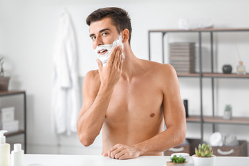 Handsome young man shaving at home