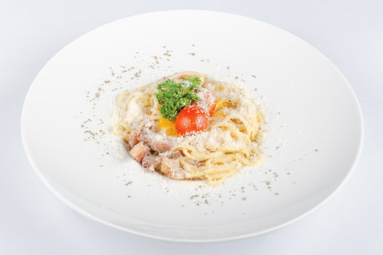 typical spaghetti alla carbonara  with raw egg and bacon. served on a white plate with grated Pecorino cheese. decorated with cherry tomato and parsley. top view