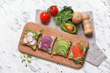 Wooden board with different tasty sandwiches on white background