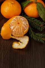 On a dark wenge-colored table lie three fresh, fragrant mandarins, one nearly peeled.