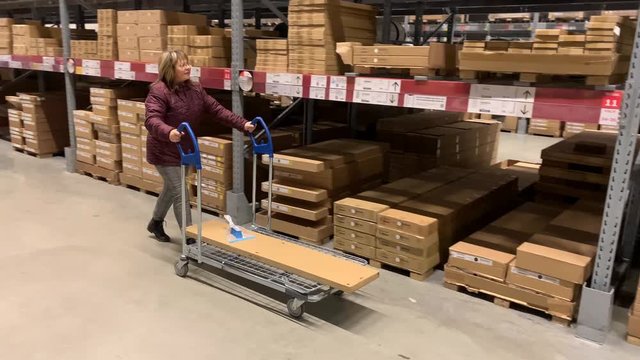 woman in a jacket carries a large shopping trolley in a self-service furniture store, a shopping concept
