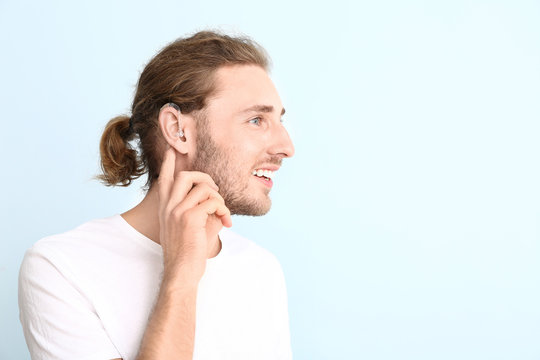 Young man with hearing aid on color background