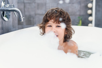 Funny little boy plays with foam in a bath.