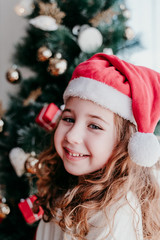 portrait of beautiful kid girl at home by the christmas tree. happy girl