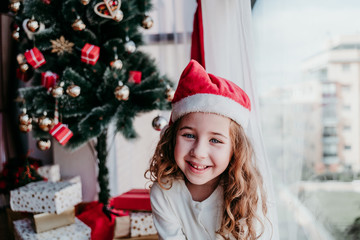 portrait of beautiful kid girl at home by the christmas tree. happy girl