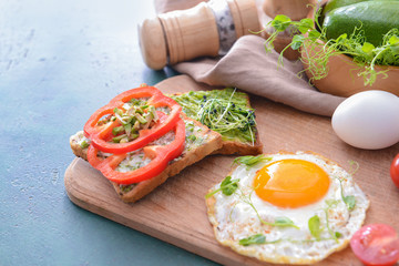 Tasty avocado sandwiches with fried egg on wooden board