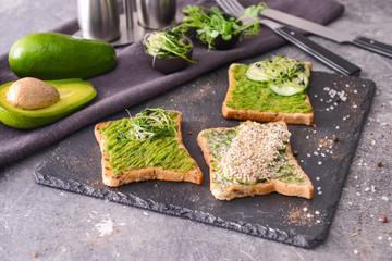 Slate plate with tasty avocado sandwiches on grey background