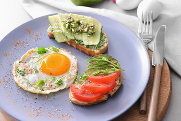 Plate with tasty avocado sandwiches and fried egg on table