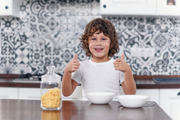 Happy boy feels happiness while eating healthy breakfast of cornflakes and milk at the kitchen.