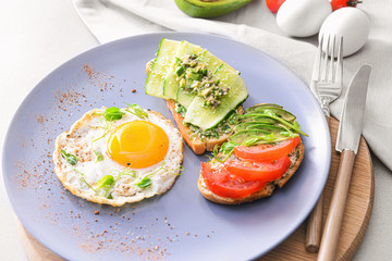 Plate with tasty avocado sandwiches and fried egg on table