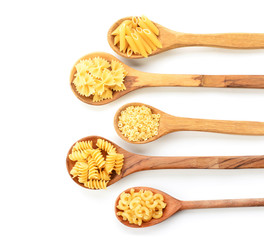 Spoons with different uncooked pasta on white background