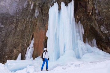 Woman hiker next to a tall frozen waterfall during a Winter hike at Seven Ladders Canyon (7 Scari)...