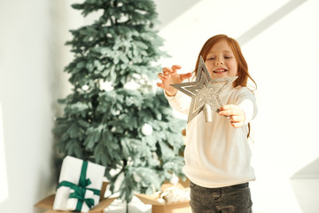 A little girl with a silver star in her hands on a Christmas tree background