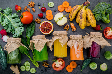 Colourful healthy smoothies and juices in bottles with fresh tropical fruit and superfoods on dark stone background with copy space.