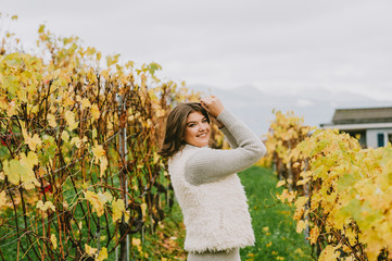 Obraz na płótnie Canvas Autumn portrait of happy young woman enjoying nice day in vineyards, wearing grey pullover and fluffy white jacket