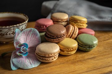 Colorful macarons, orchid flower and a cup of tea put on wood table. Colorful macarons french dessert