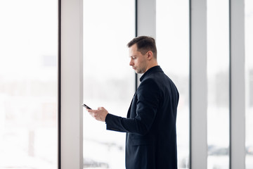 Business man using mobile phone app in airport. Young business professional man texting smartphone walking inside office building or airport terminal. Handsome man wearing stylish suit jacket indoors.