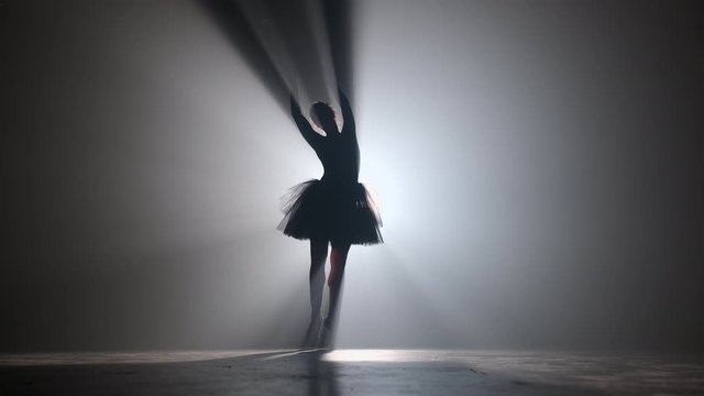 Solo performance by ballerina in tutu against backdrop of luminous spotlight 