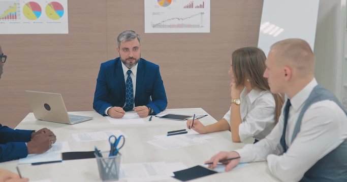 Вirector of the company tells his colleagues new goals and objectives, a startup. Business partners listen to the head of the corporation. Side span of the camera.