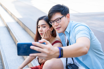 A loving couple tourist is taking a selfie on their smartphone in the city center,They are looking at the camera holding each other,Capturing bright moments.