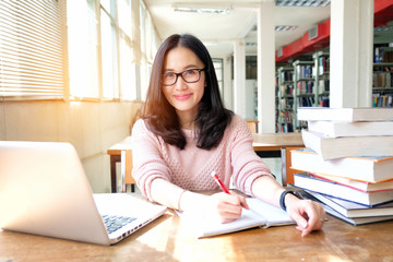 Young woman taking note and using laptop while studying in library