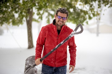 Male holding a snow shovel and wearing a red jacket while smiling at the camera