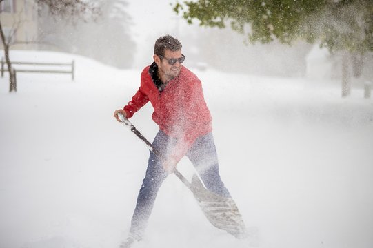 Male Wearing A Red Jacket And Shoveling Snow With A Blurred Background