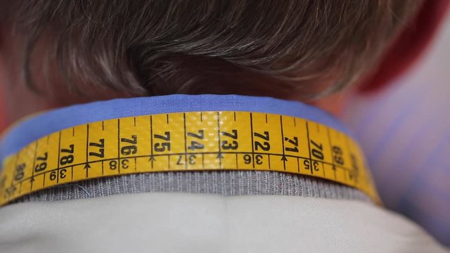 Close up of the back of a tailors neck with tape measure whist he pins a new garment on a man
