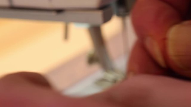 Extreme close up tailor threading a needle with sewing machine in the background