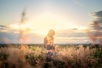 Trendy girl in stylish summer dress feeling free in the field with flowers in sunshine.