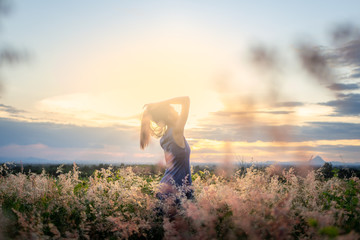 Trendy girl in stylish summer dress feeling free in the field with flowers in sunshine.