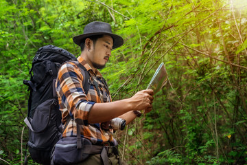 man traveler with backpack and map searching directions in the forest