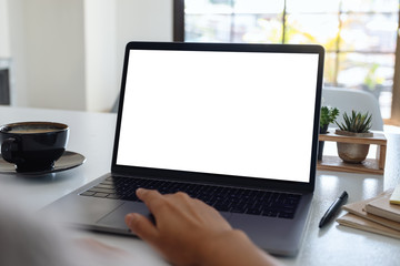 Fototapeta premium Makieta obrazu ręki dotykającej touchpada laptopa z pustym białym ekranem pulpitu z filiżanką kawy na drewnianym stole