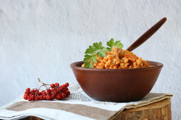 Delicious traditiional barley porridge with chicken, vegetables and parsley in ceramic bowl on textile napkin and wooden table