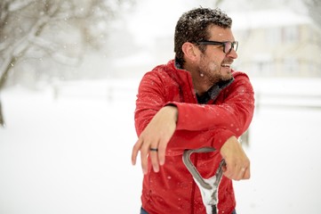 Closeup shot of a male with his hands on the snow shovel and wearing a red jacket on a snowy day