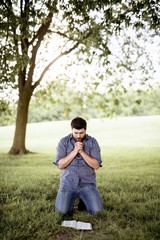 Vertical shot of a male on his knees with the bible in front of him while praying