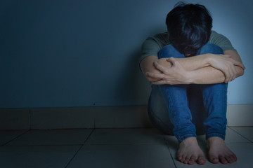 sad man hug his knee and cry sitting alone in a dark room. Depression, unhappy, stressed and...