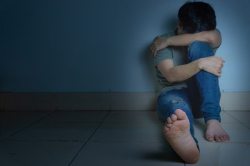 Fototapeta premium sad man hug his knee and cry sitting alone in a dark room. Depression, unhappy, stressed and anxiety disorder concept