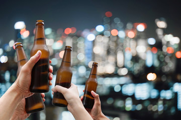 Hands holding beer bottles and happy enjoying harvest time together to clinking glasses at outdoor party on beautiful bokeh night light background.Celebration drinking beer in pub orbar.         