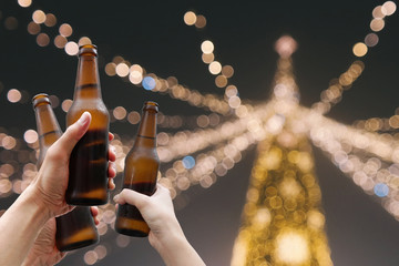 Hands holding beer bottles and happy enjoying harvest time together to clinking glasses at outdoor party on beautiful bokeh night light background.Celebration drinking beer in pub orbar.         
