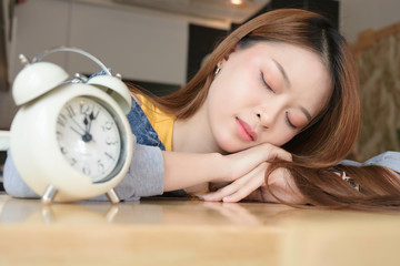 Beautiful young asian woman long hair sleeping with white alarm clock on wooden table in room background.
