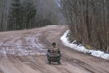 a man in camouflage, a hunter, sitting on a dirty road, looking for prey