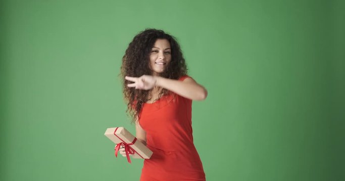 Joyful woman holding Christmas present and dancing over green background