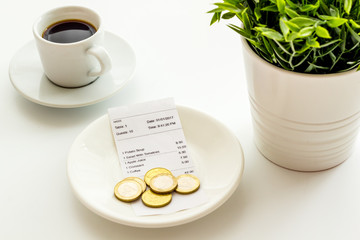 Pay restaurant bill by cash. Reciept and coins on plate on white background