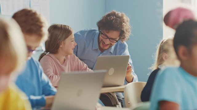 Elementary School Computer Science Class: Smart Girl Uses Laptop Computer, Friendly Teacher Helps Her by Explaining Lesson and Asignment. Children Getting Modern Education