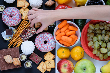 Healthy and unhealthy food concept, fruits and vegetables vs donuts, sweets and chocolate with woman's hand. Top view