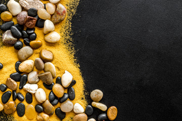 Resort or vacation concept. Sea stones and sand on black background top-down frame copy space