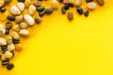 Sea rest, summer vacation concept. Stones and sand on yellow background top-down frame copy space