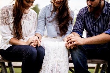 Closeup shot of people sitting and holding hands while praying with a blurred background