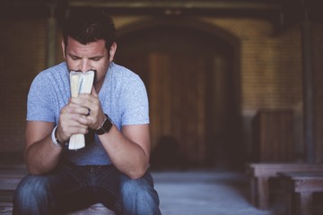 Closeup shot of male holding the bible in front of his mouth while praying with blurred background